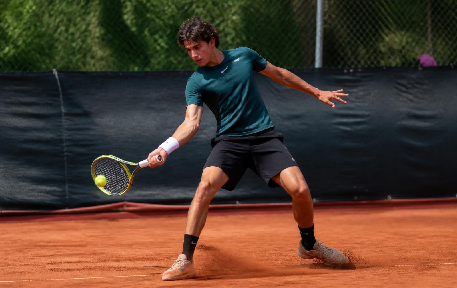 A tennis player mid-rally on an outdoor clay court in afternoon light
