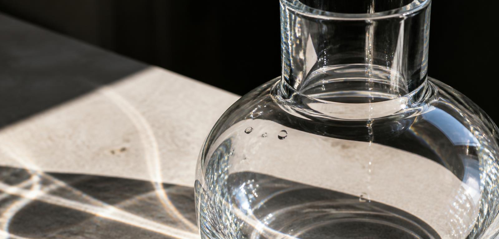 Macro detail of heavy crystal-clear glass refracting daylight onto pale stone