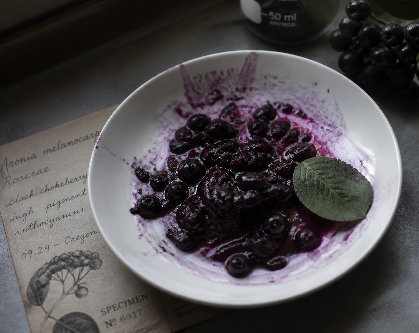 Crushed aronia berries staining a white dish deep violet, showing the anthocyanin pigment